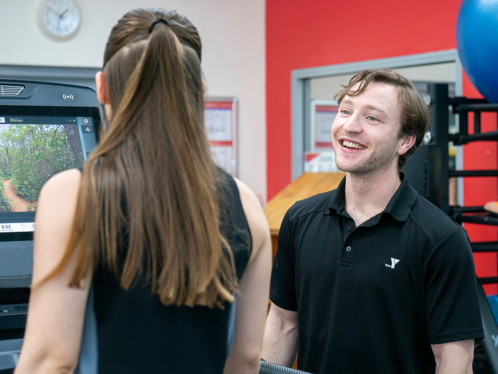 Smiling gym staff member greeting client at modern fitness facility front desk