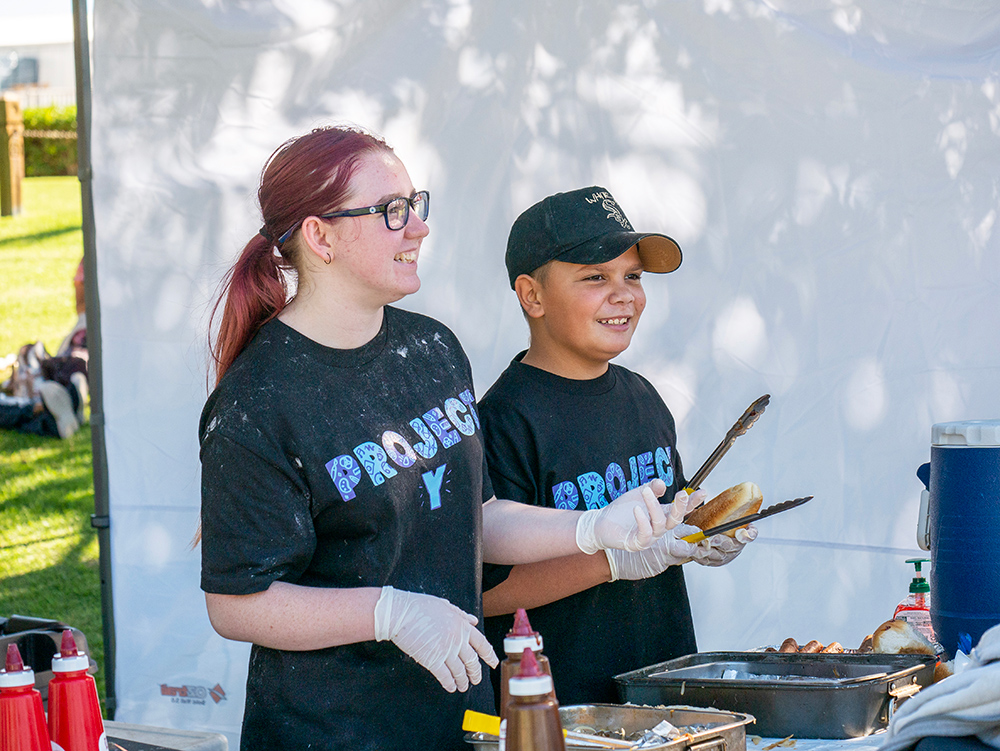Youth volunteers in Project Y shirts serving food at outdoor community BBQ event