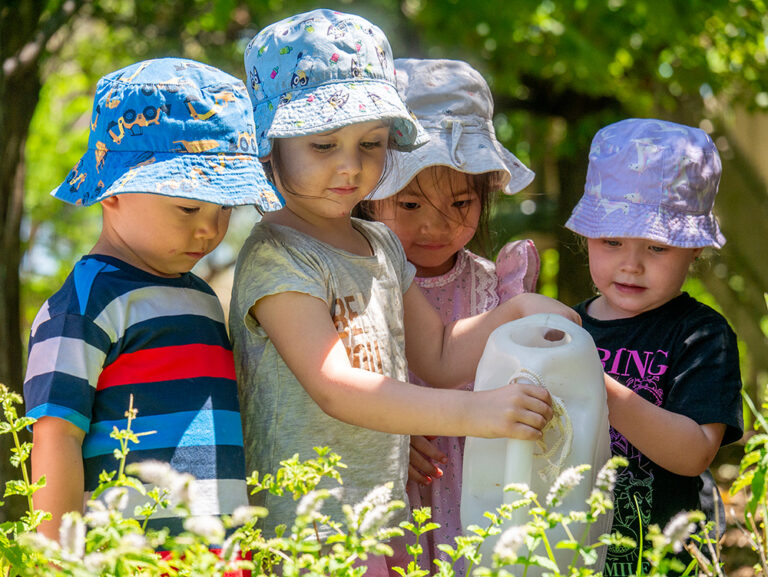 A group of young children wearing hats and watering plants in the garden.
