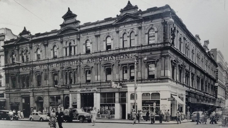 Vintage black and white photo of the Young Men's Christian Association building on a busy city street corner.