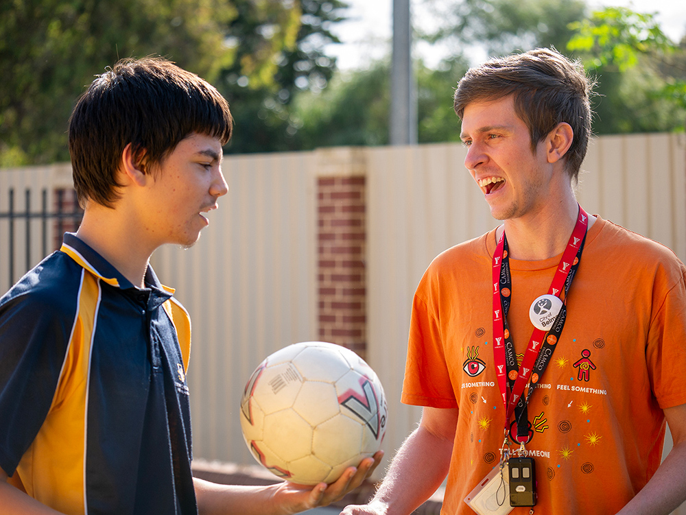 Youth program coordinator engaging with student holding soccer ball during school activity