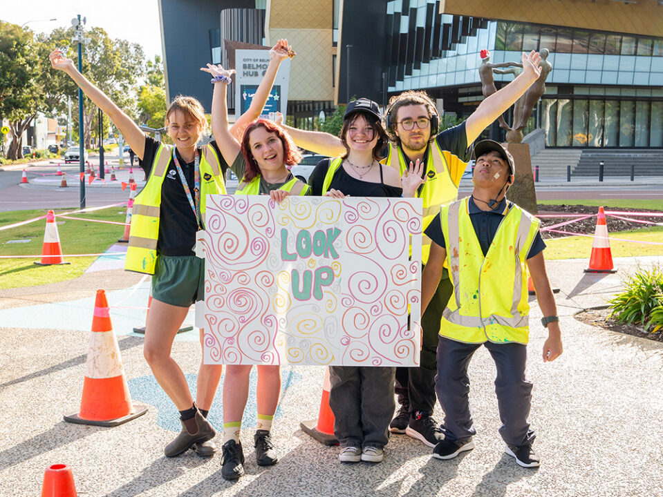 Group of young people and youth workers smiling and excited holding up a sign outside