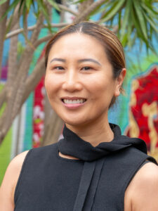 Smiling Y WA Board member Eva in a black top, photographed outdoors against a colourful mural backdrop.