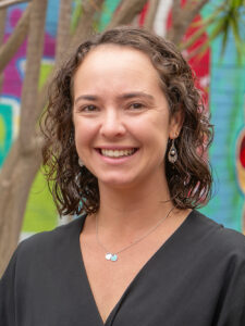 Smiling Y WA Board member Tegan in a black top, photographed outdoors against a colourful mural backdrop.