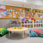 Early learning centre play area with floor cushions, low table, storage cubbies and display boards