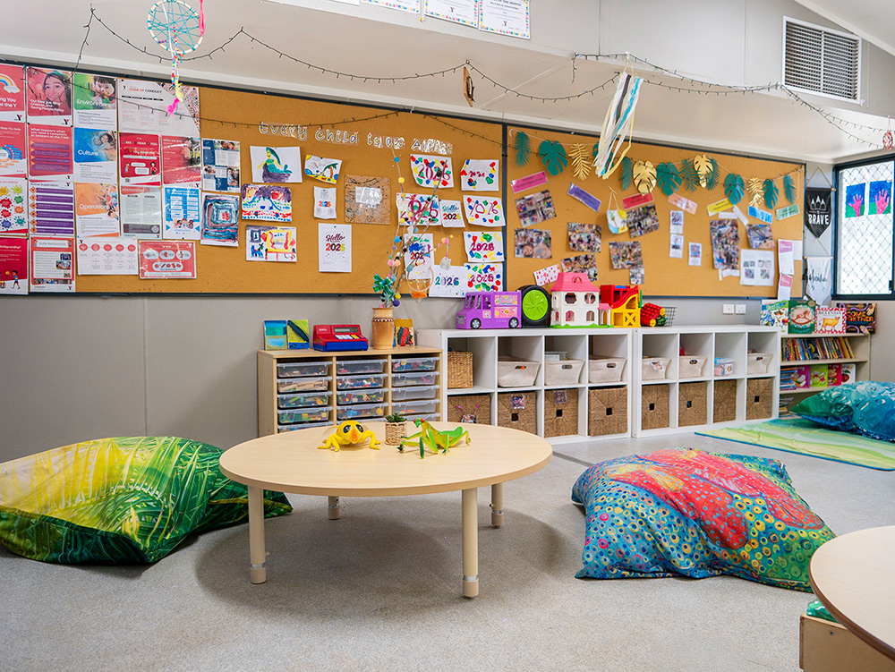 Early learning centre play area with floor cushions, low table, storage cubbies and display boards