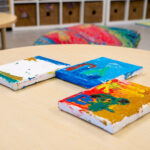 Colorful canvas paintings created by children displayed on table in early learning classroom