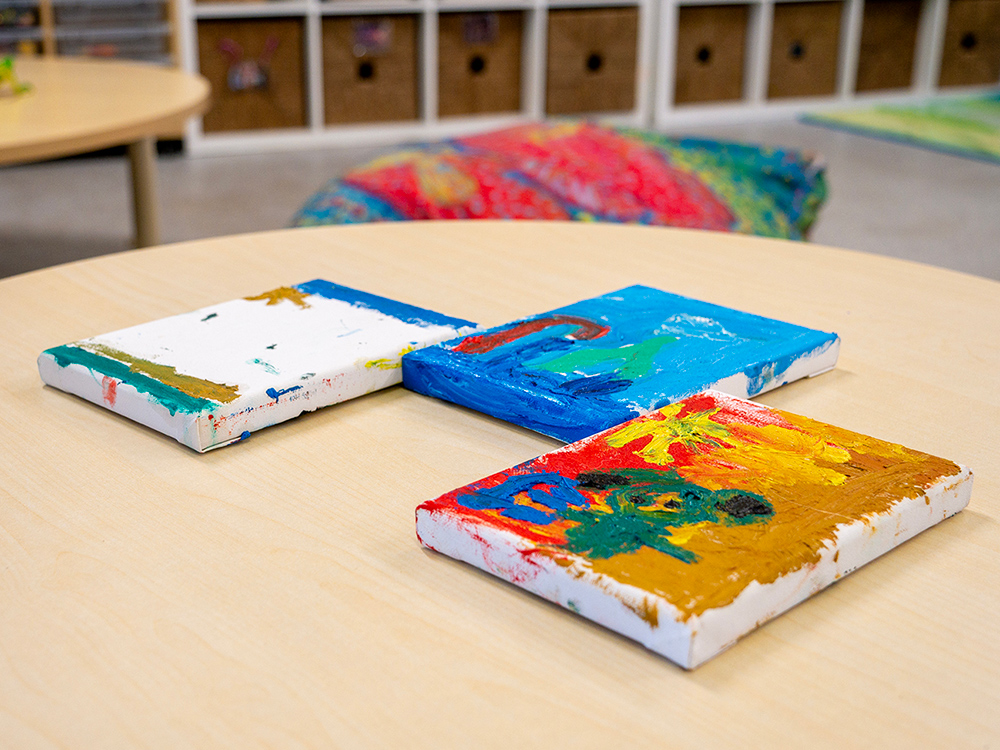 Colorful canvas paintings created by children displayed on table in early learning classroom