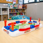 Tabletop football game toy on table in early learning room with books and storage shelves