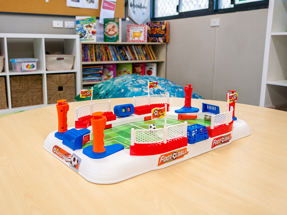 Tabletop football game toy on table in early learning room with books and storage shelves