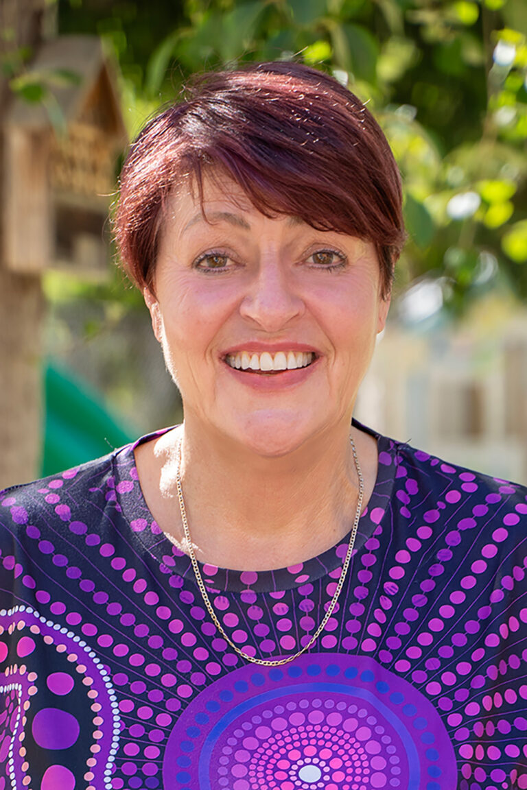 Professional headshot of smiling OSHC supervisor in purple Indigenous-design shirt outdoors