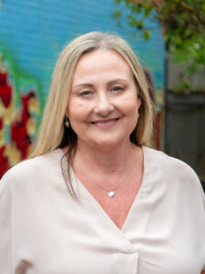 Smiling Y WA executive in a cream top, photographed outdoors against a colourful mural backdrop.