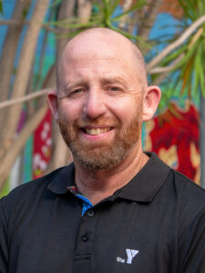 Smiling Y WA executive in a black Y polo shirt, photographed outdoors against a colourful mural backdrop.