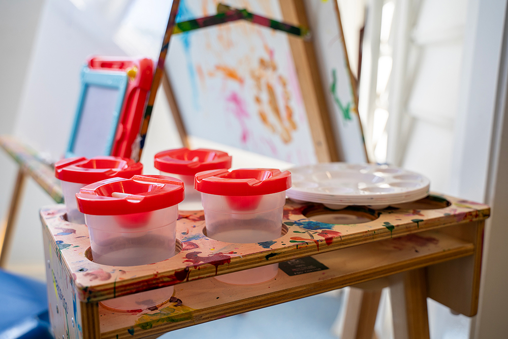 Paint containers and brushes arranged on splattered easel at OSHC creative arts station