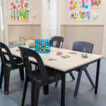 OSHC games table with board games and chairs beneath colorful children's handprint artwork