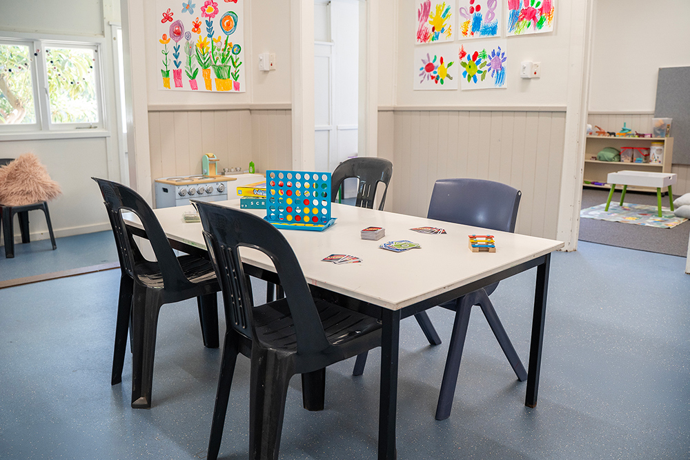 OSHC games table with board games and chairs beneath colorful children's handprint artwork