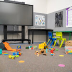 OSHC activity room with screen, colorful chairs, floor toys and children's artwork on walls
