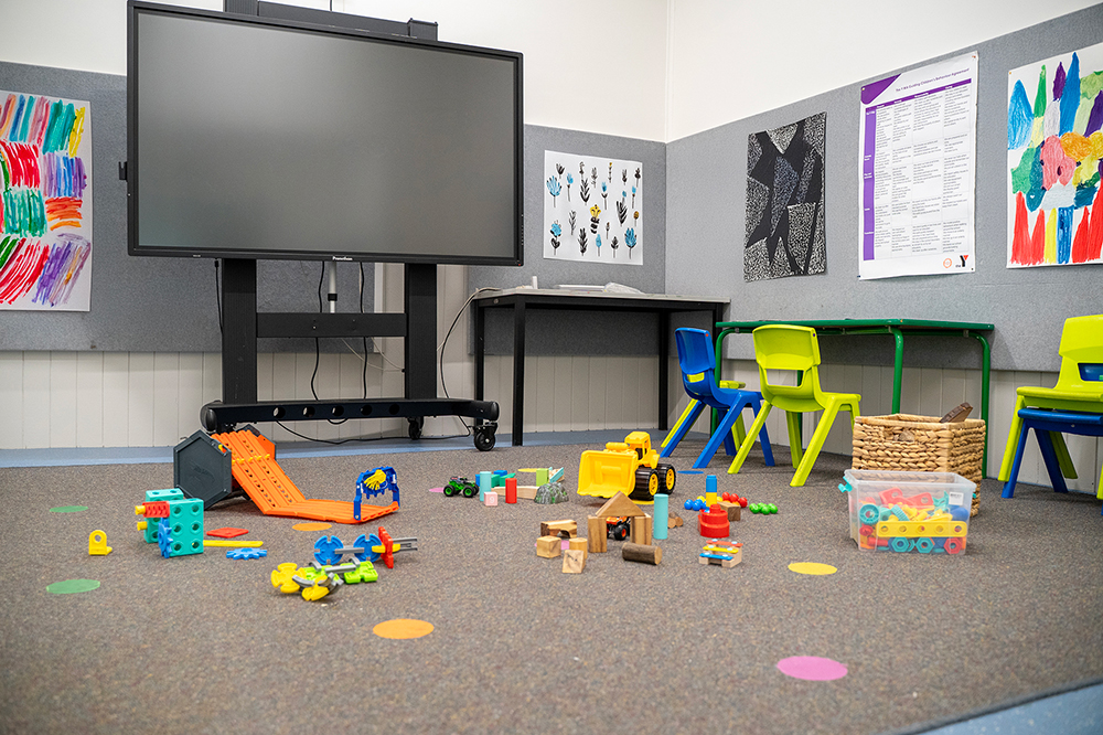 OSHC activity room with screen, colorful chairs, floor toys and children's artwork on walls
