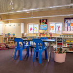 OSHC activity room with blue plastic chairs, craft storage, colorful letter displays and floor cushions