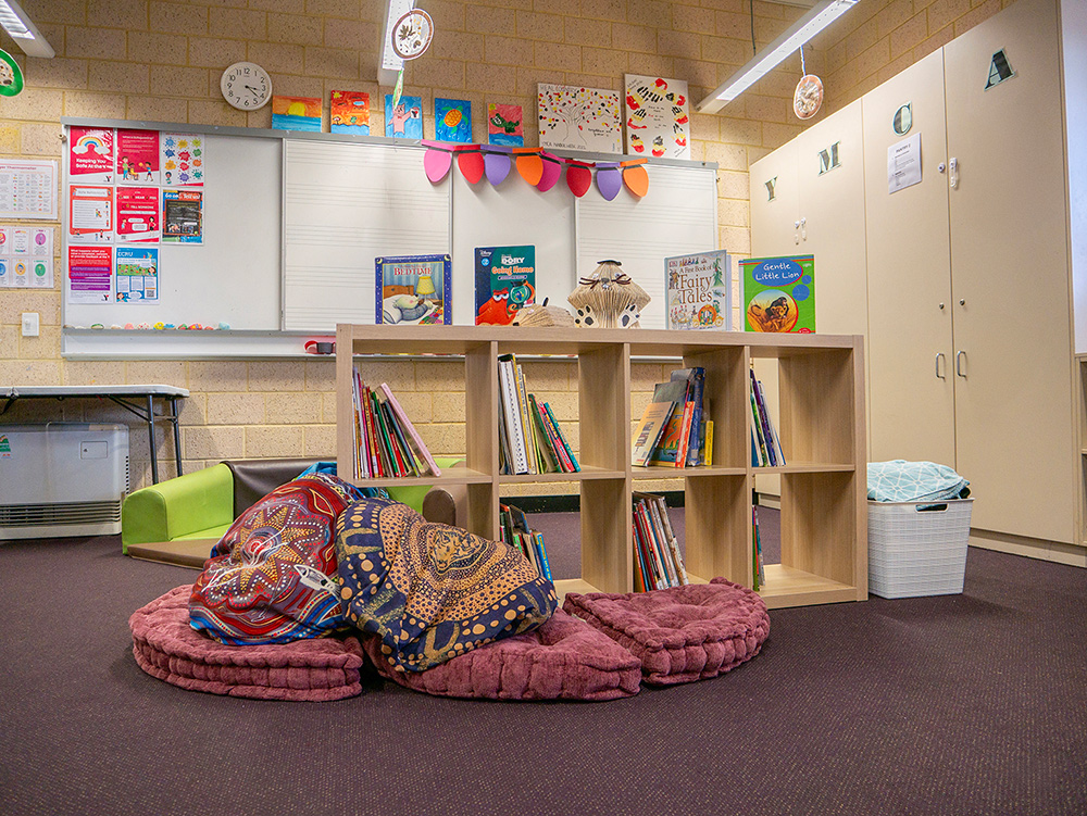 OSHC reading nook with floor cushions, book shelves, whiteboard and children's artwork displays