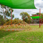 OSHC outdoor play space with climbing dome, shade sails and grassed area