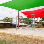 OSHC playground with climbing equipment and sandpit under green and red shade sails