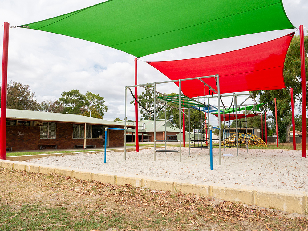 OSHC playground with climbing equipment and sandpit under green and red shade sails