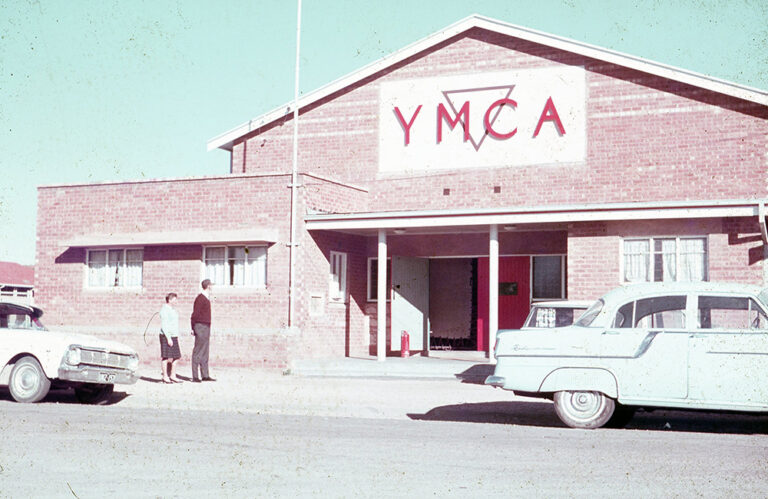 Vintage colour photo of the Kalgoorlie YMCA brick building with classic cars parked outside.