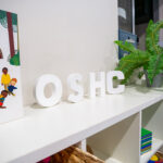 OSHC sign display with children's book and plant on white shelf unit