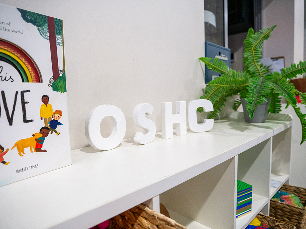 OSHC sign display with children's book and plant on white shelf unit