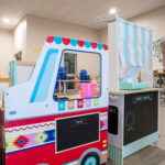 Colorful wooden play food truck and puppet theater set in bright early learning classroom