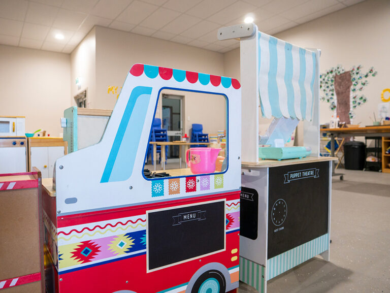 Colorful wooden play food truck and puppet theater set in bright early learning classroom