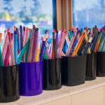 Row of pencil holders filled with colorful markers and pens at OSHC art station