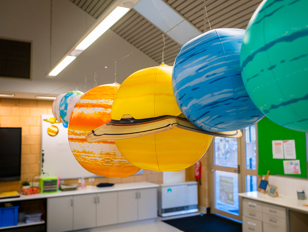 Colourful hanging solar system planet models suspended from OSHC classroom ceiling