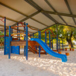 Large covered playground with blue climbing equipment and slide over sandpit at OSHC