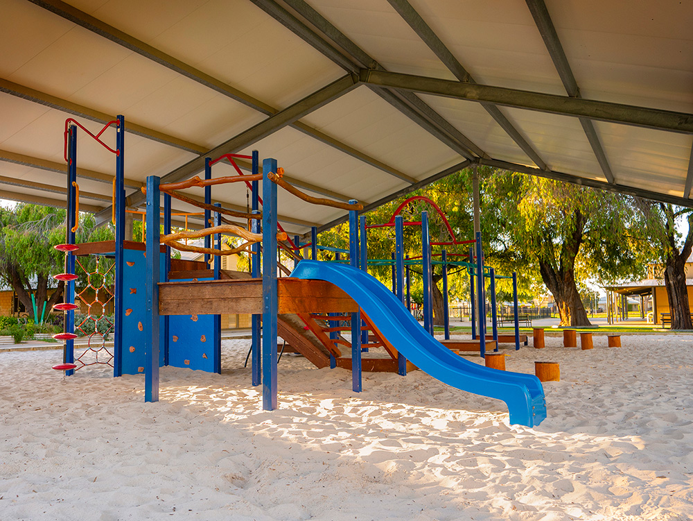 Large covered playground with blue climbing equipment and slide over sandpit at OSHC