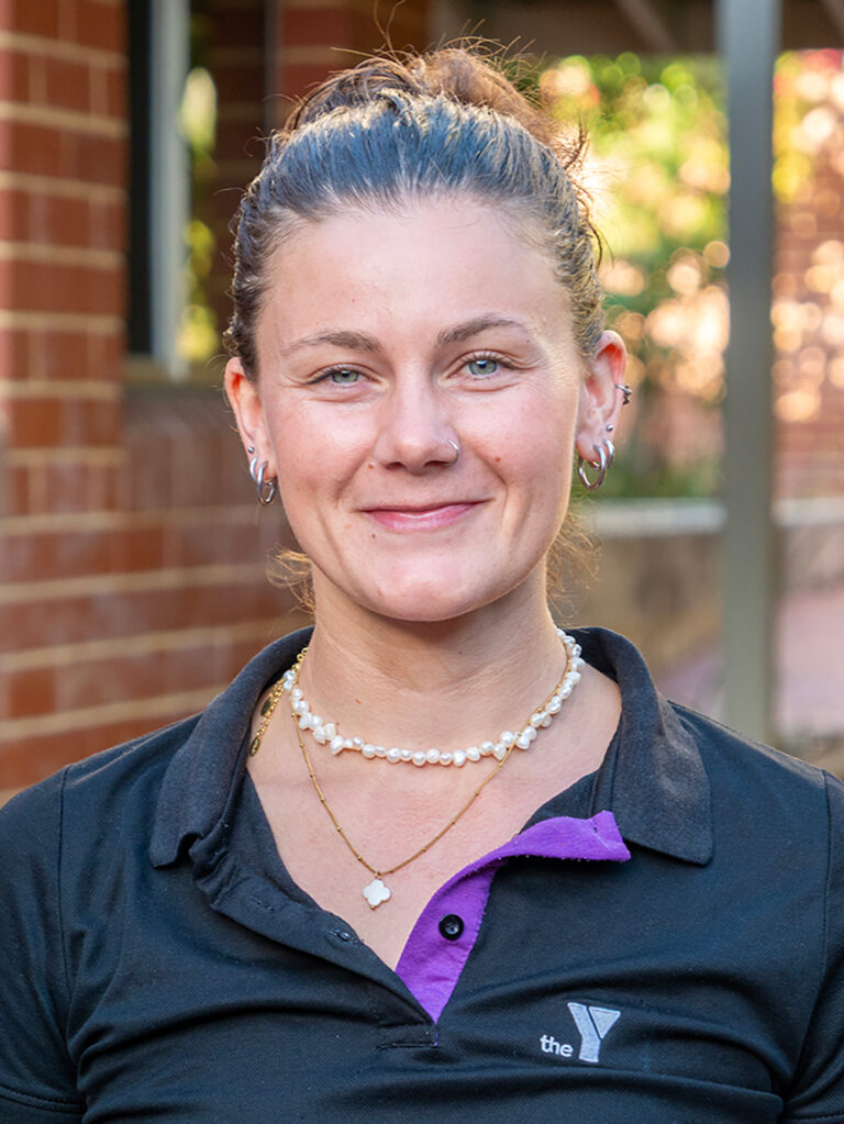 A smiling Y WA staff member in a black and purple Y polo shirt outdoors.