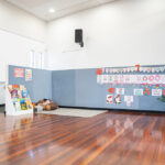 OSHC hall reading corner with bookshelf and children's poppy artwork displayed on wall