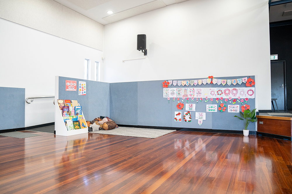 OSHC hall reading corner with bookshelf and children's poppy artwork displayed on wall