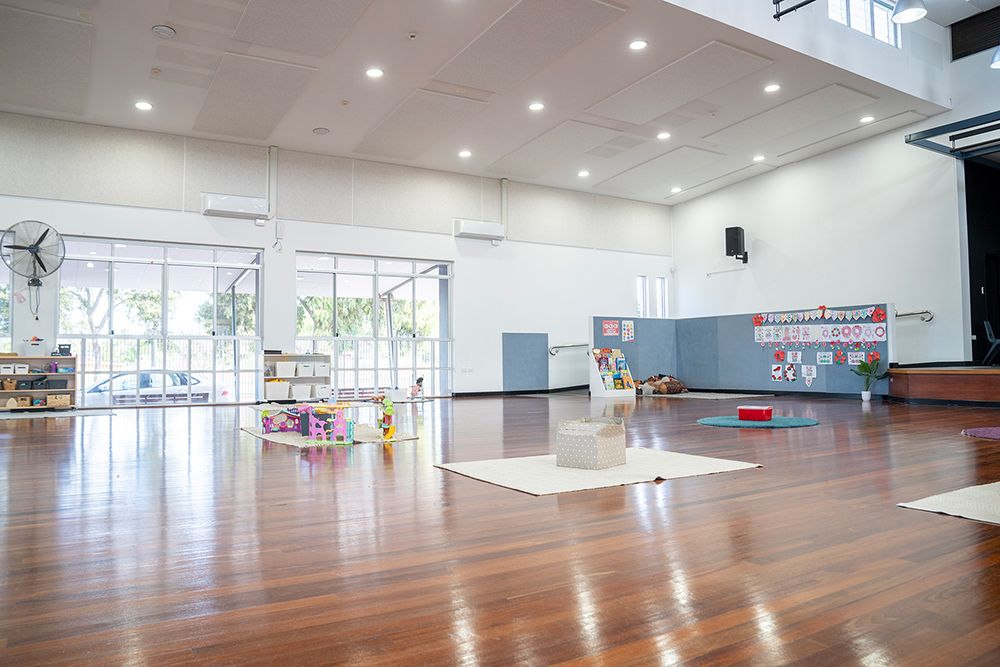 Spacious OSHC hall with polished timber floors, play mats and display boards