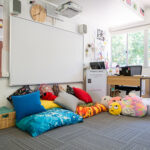OSHC relaxation corner with colourful floor cushions, soft toys, whiteboard and children's artwork
