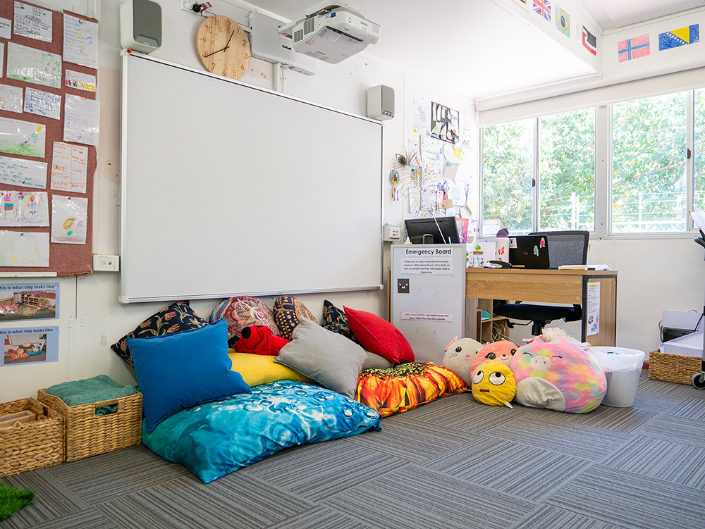 OSHC relaxation corner with colourful floor cushions, soft toys, whiteboard and children's artwork