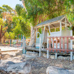 Natural OSHC playground with wooden cubby house, logs and shade trees