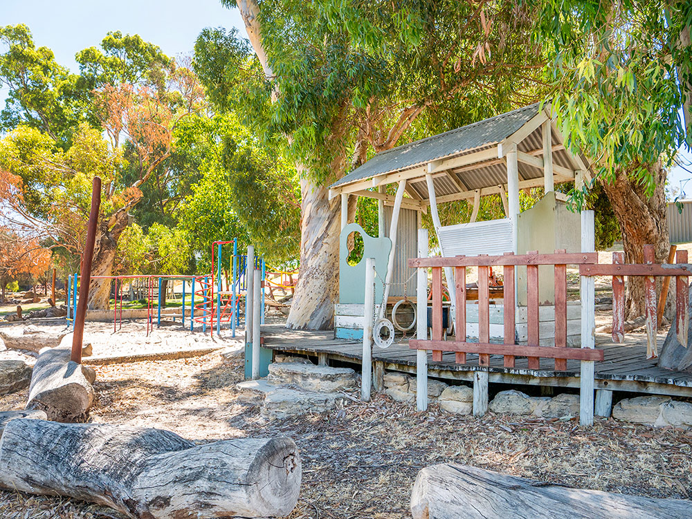 Natural OSHC playground with wooden cubby house, logs and shade trees