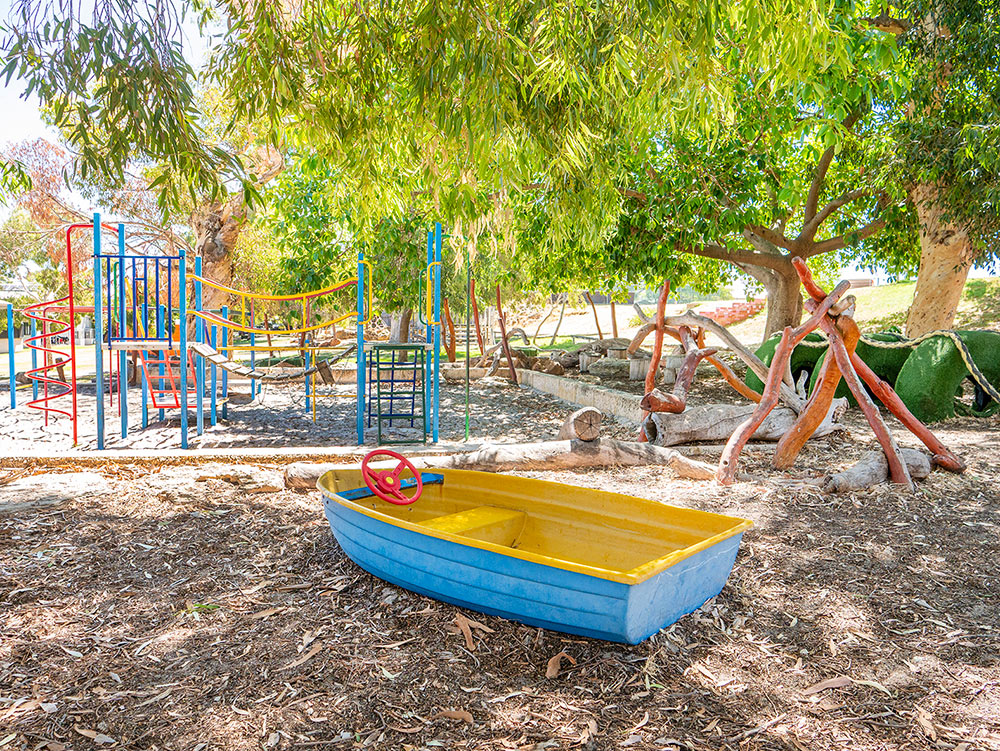 OSHC nature play area with boat sandpit, wooden climbing sculpture and colourful equipment
