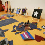 A table displaying young people's creative artworks including small painted canvases on mini easels and denim fabric craft pieces during a youth art activity