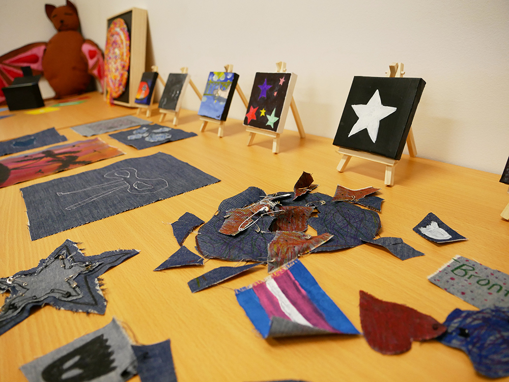 A table displaying young people's creative artworks including small painted canvases on mini easels and denim fabric craft pieces during a youth art activity