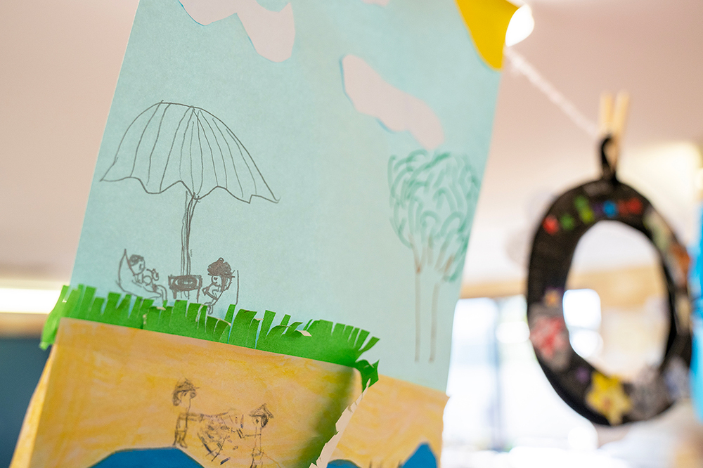 Children's paper craft showing outdoor play scenes and stained glass ornament at OSHC