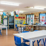 Bright OSHC classroom with white tables, blue chairs, children's artwork and activity areas