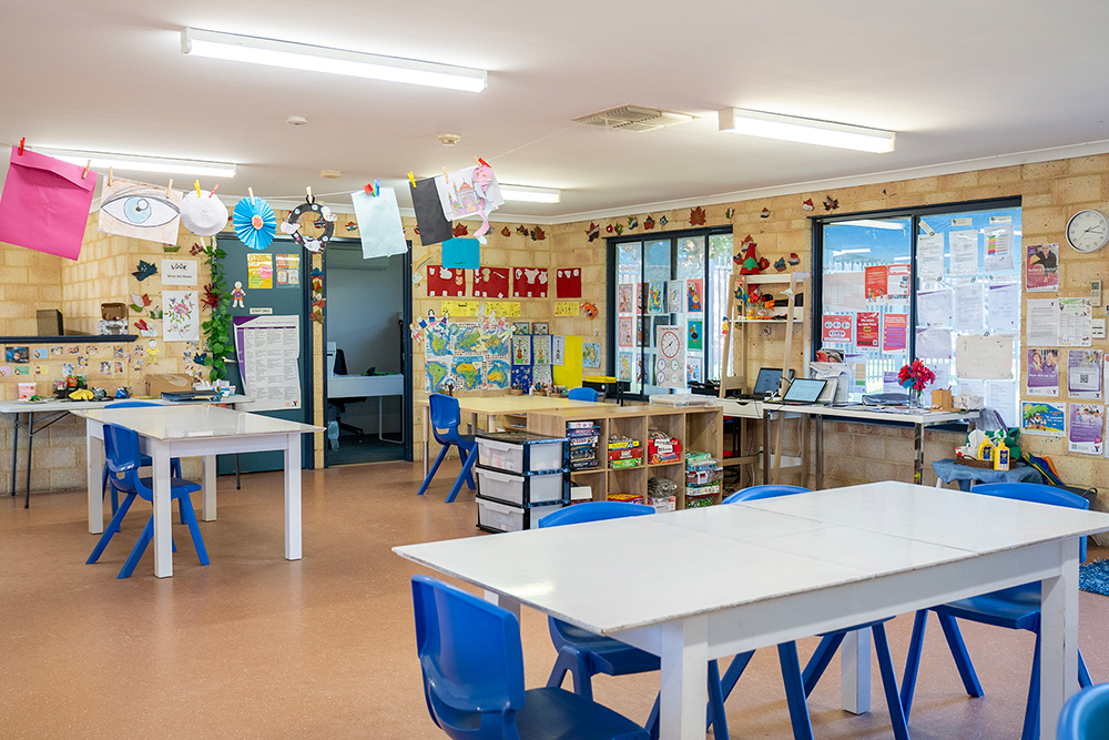 Bright OSHC classroom with white tables, blue chairs, children's artwork and activity areas